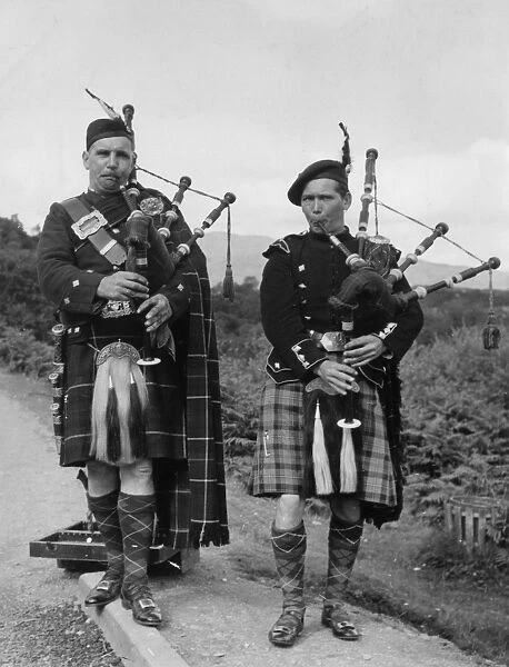 Two bagpipers on a road in the Trossachs, Scotland