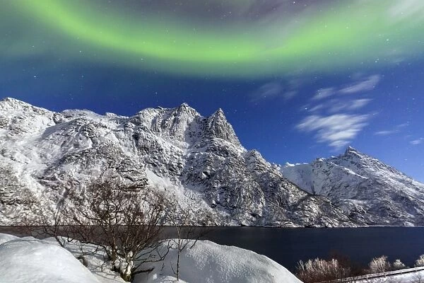 Northern Lights (aurora borealis) illuminate the snowy peaks and the blue sky during a starry night