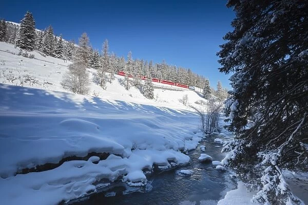 Rhaetian Railway on the Chapella Viadukt surrounded by snowy woods, Canton of Graubunde