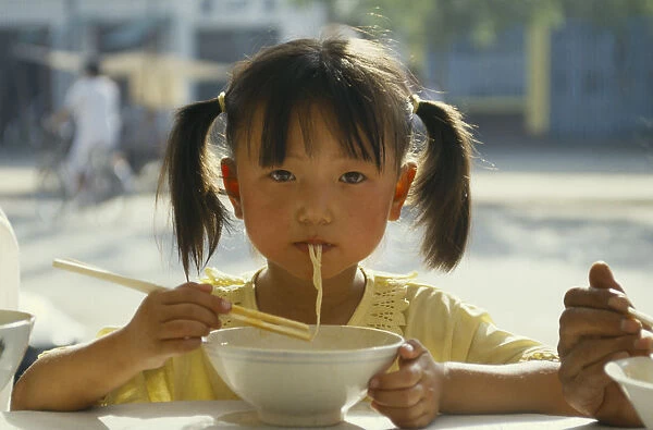 10002698. CHINA Guizhou Guiyang Pony tailed young girl eating noodles
