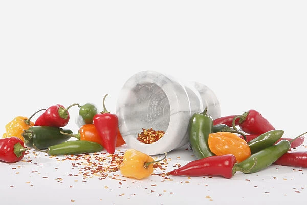 Different types of fresh chilli peppers arranged around a mortar, with crushed, dried chilli peppers inside and scattered around it