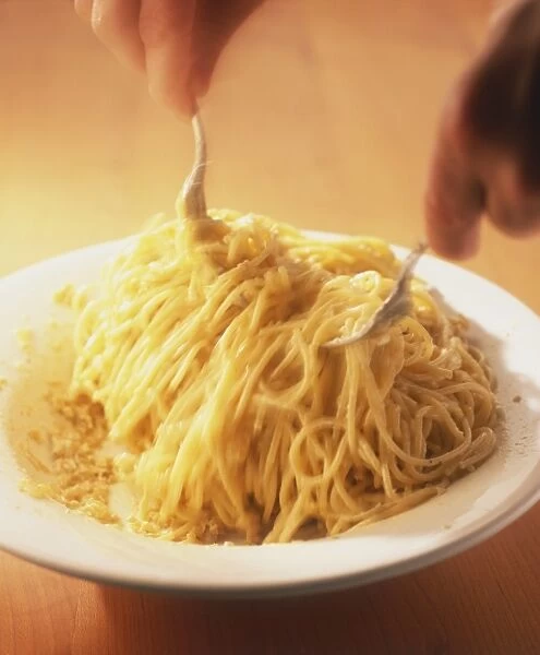 Spaghetti being tossed in a cream sauce with two forks