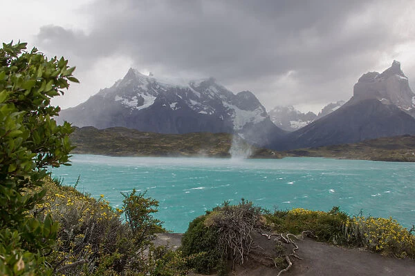 The wind whips up waves and a waterspout across the cold waters of Lake Pehue to the snow-capped mountain peaks of the Torres del Paine National Park in the Magallanes Region of Patagonia, Southern Chile