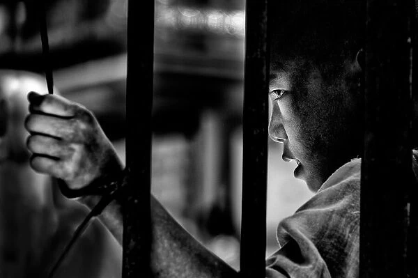A young monk behind the bars of a Buddhist school