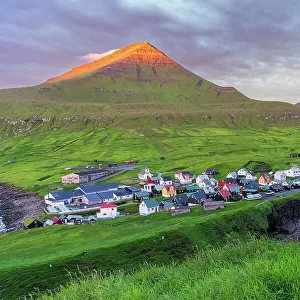 Colorful houses of the village of Gjogv with the mounatins lit by the early sun, sunrise view, Eysturoy island, Faroe islands, Denmark, Europe
