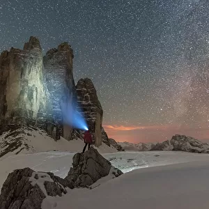 Hiker with head torch views the Tre Cime di Lavaredo on a starry night with the Milky Way, winter view, Tre Cime di Lavaredo (Lavaredo peaks), Sesto (Sexten), Dolomites, South Tyrol, Italy, Europe