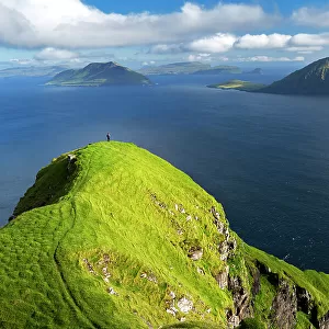 Hiker walks on top of a tall cliff overlooking the ocean, Nordradalur, Streymoy island, Faroe islands, Denmark, Europe
