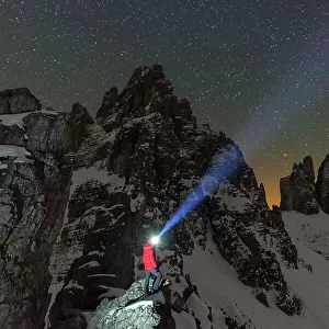 Man with head torch illuminates the starry sky over the snowy Paterno mountain and Tre Cime di Lavaredo (Lavaredo peaks), Sesto (Sexten), Dolomites, South Tyrol, Italy, Europe