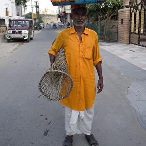 Man in yellow kurta with tray of snacks on his head and table under his arm
