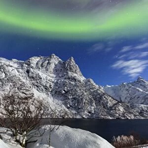 Northern Lights (aurora borealis) illuminate the snowy peaks and the blue sky during a starry night