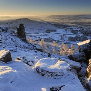 Snow on millstone lit by sunrise, Curbar and Baslow Edge with misty hills and wintry trees, Peak District, Derbyshire, England, United Kingdom, Europe