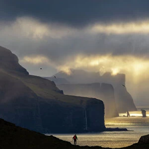 A trekker observes the scenic view in front of him from Kallur Lighthouse at sunset, Kalsoy, Faroe Islands, Denmark (MR)