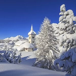 The winter sun illuminate the snowy landscape and the typical church Maloja Canton