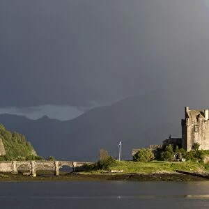 View of restored castle on tidal island in sea loch with rainbow, in evening sunlight, Eilean Donan Castle, Loch Duich