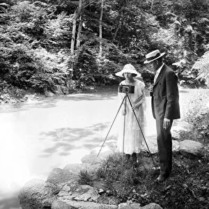 COUPLE WITH CAMERA, c1915. American couple with a camera by a stream, c1915