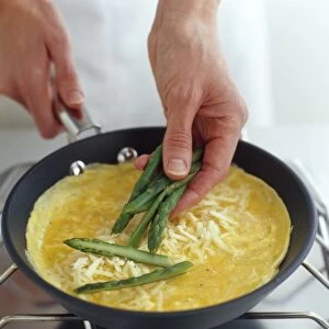 Asparagus spears being laid over omelette cooking in frying pan, high angle view