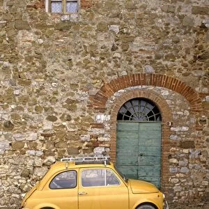 Italy, Tuscany, yellow Fiat 500 parked outside entrance to old stone house, close-up