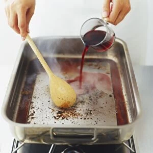 Pouring red wine into a heated pan and using spoon to scrape off dark spots from bottom of pan