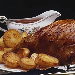 Roast pork served with roasted potatoes and a gravy boat, side view