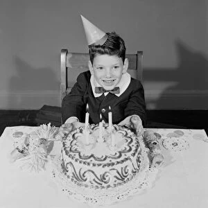 Boy (6-7) sitting at table with birthday cake, portrait