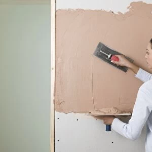 Woman holding a plastering hawk and spreading plaster on to a wall with a trowel