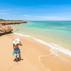 Woman with sarong and straw hat looking away on the beach at Osprey Bay, Cape Range National Park, Exmouth, Western Australia