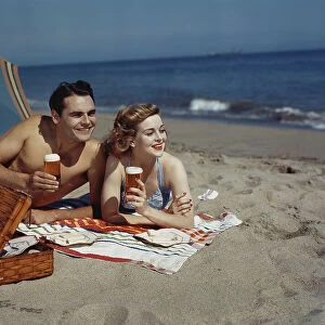 Young couple lying on beach with beer, smiling