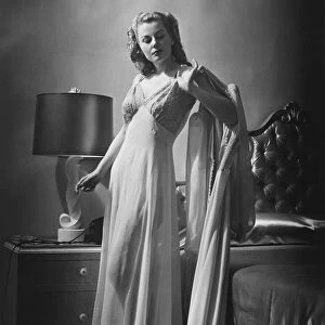 Young woman standing by bed wearing dressing gown, (B&W)