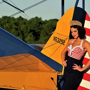 1940s style pin-up girl leaning on the tail fin of a Stearman biplane