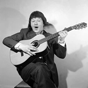 Comedian Benny Hill pictured at home wearing a wig and playing the guitar May 1958