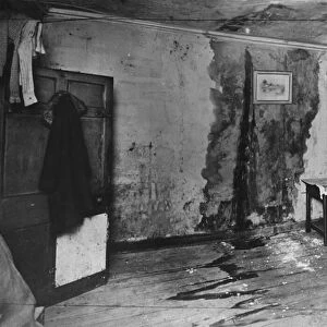 A man inside slum housing in Liverpool inspect a large damp patch on the wall. circa 1935