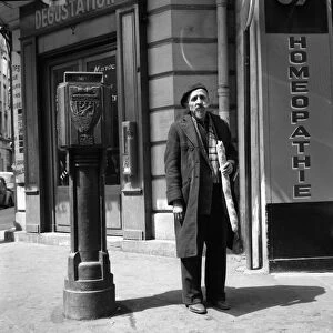 An old Parisian man next to a homeopathic shop Paris May 1960 holding a baguette
